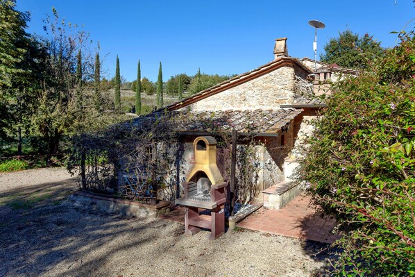 Un edificio de piedra con chimenea, rodeado de árboles y vegetación.