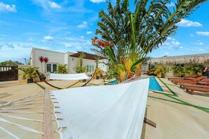 A poolside area with a hammock, lounge chairs, and a thatched-roof structure. - EVA Aruba Boutique Resort & SPA (Savaneta)