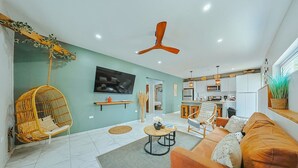 A modern living room with a sofa, a hanging chair, a TV, and a ceiling fan. - EVA Aruba Boutique Resort & SPA (Savaneta)