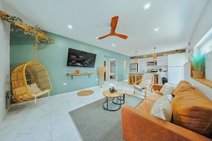 A modern living room with a sofa, a hanging chair, a TV, and a ceiling fan. - EVA Aruba Boutique Resort & SPA (Savaneta)