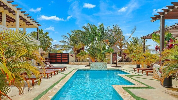 A rectangular swimming pool with a stone border, surrounded by lounge chairs and tropical plants. - EVA Aruba Boutique Resort & SPA (Savaneta)