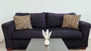 Ein dunkelbraunes Sofa mit gemusterten Kissen, eine kleine weiße Vase auf einem dunklen Tisch und zwei gerahmte Blumenbilder an der Wand.