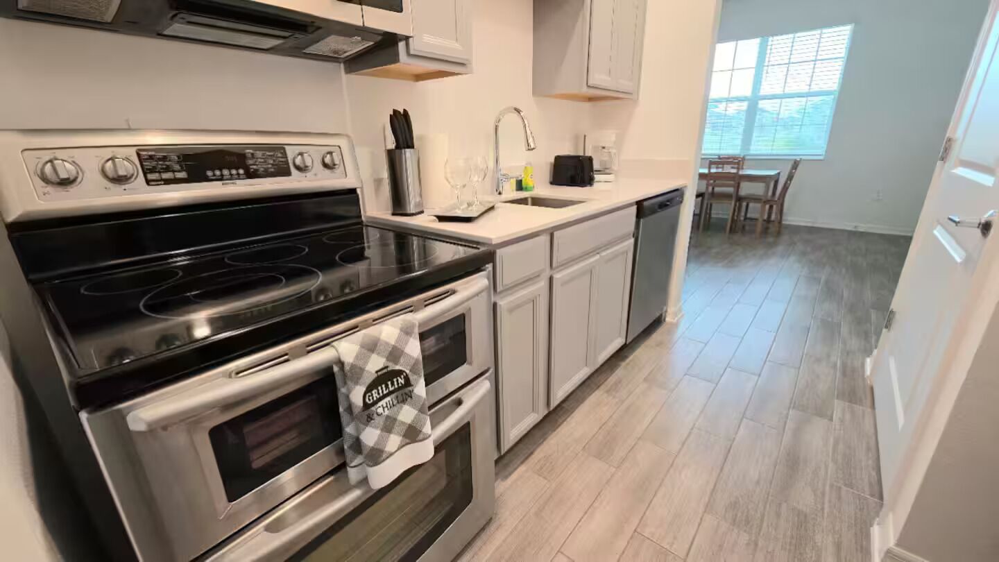 A modern kitchen with stainless steel appliances, a dishwasher, and a dining area with a window.