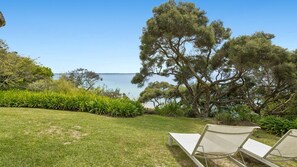 A grassy area with two white lounge chairs facing a large tree and a view of the sea. - Somerset - Portsea - Coastal Escape with Private Beach Access (Portsea)