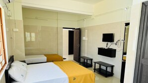 A hotel room with two beds, a small table, a bench, a TV, and a bathroom door.