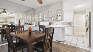 Una cocina moderna con armarios blancos, una mesa de comedor de madera y un ventilador de techo.