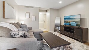 Una sala de estar moderna con un sofá seccional, una mesa de centro de madera oscura, un televisor de pantalla plana sobre un mueble de madera oscura y un cuadro grande en la pared.