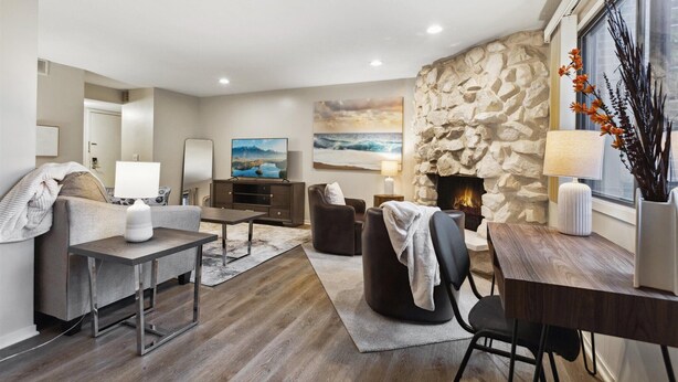Una sala de estar moderna con chimenea de piedra, un sofá gris, una mesa de centro y un comedor con mesa y sillas de madera.