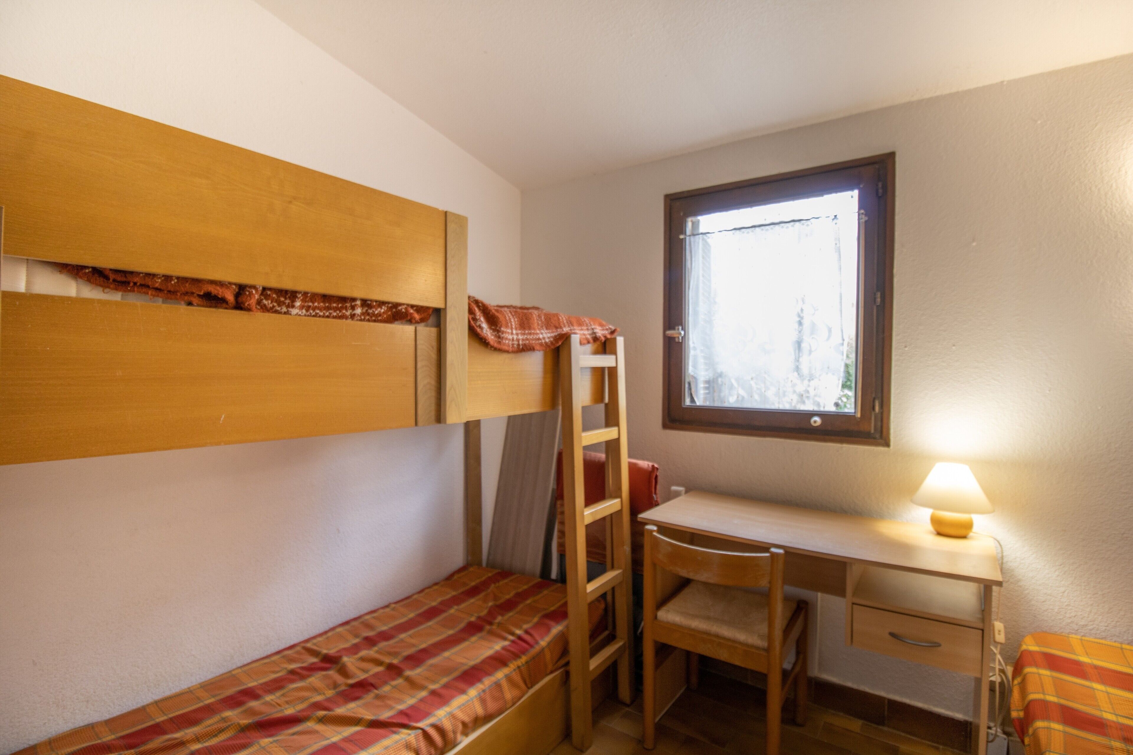 Una piccola sistemazione con una sola stanza, dotata di un letto a castello, una scrivania, una sedia e una finestra.