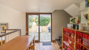 Ein Zimmer mit einem Holzesstisch, einem roten Schrank mit Küchenutensilien, einer Tür, die auf eine Terrasse mit Grill führt, und einem Bilderrahmen an der Wand.