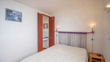 Una camera da letto con un letto, un comodino con una sveglia, un quadro appeso al muro e una porta che dà su un bagno.
