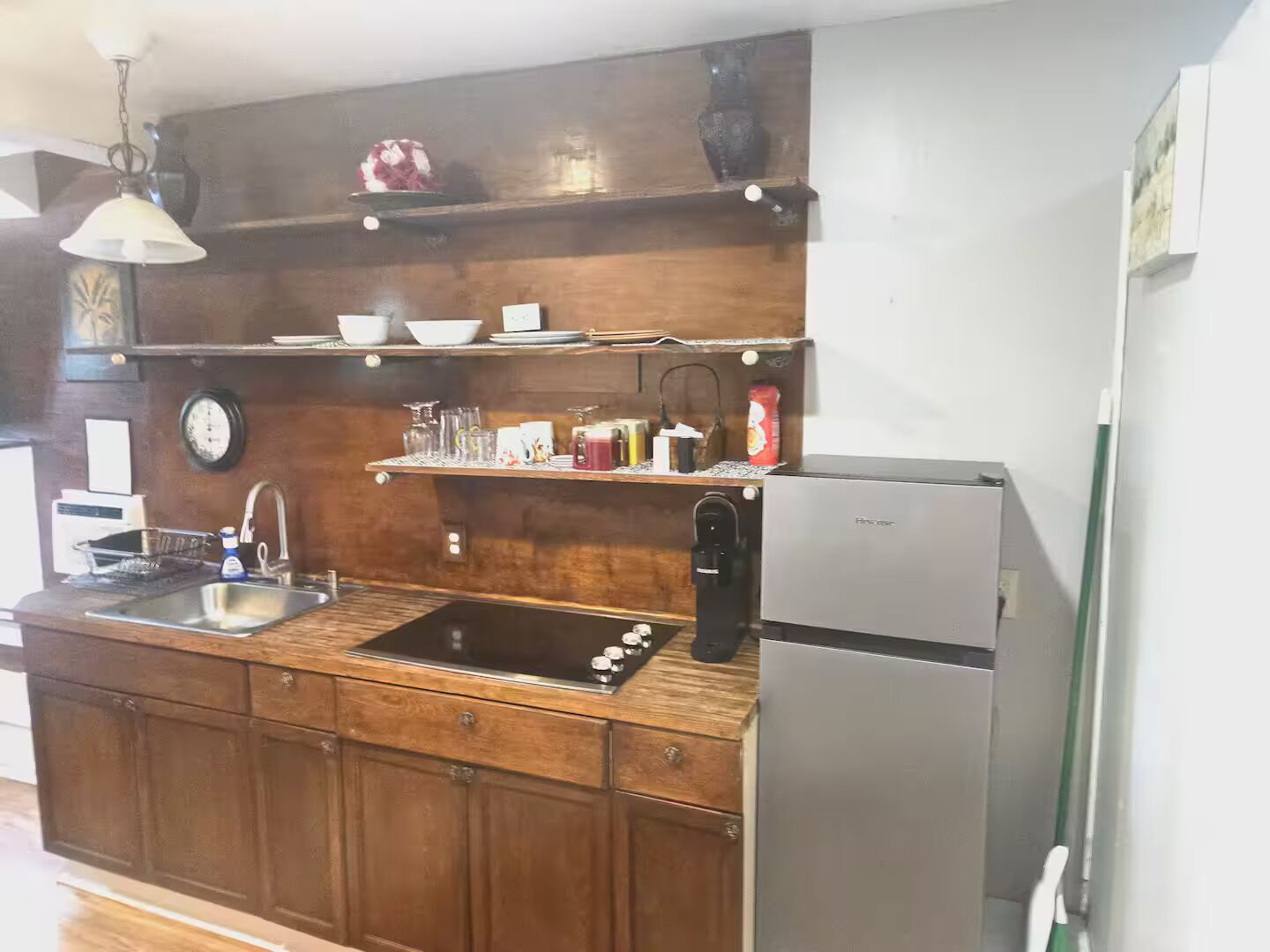 A kitchen with wooden cabinets, a stainless steel refrigerator, a sink, and various kitchen items on shelves.