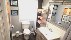 Ein Badezimmer mit Toilette, Waschbecken, Spiegel und Regalen mit Handtüchern.