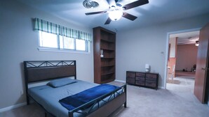 A bedroom with a bed, a ceiling fan, a window with curtains, a bookshelf, and a dresser.