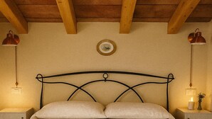 A bedroom with a wooden ceiling, a metal headboard, two bedside lamps, and a bedside table with a candle. - OLD RENOVATED COTTAGE NESTLED IN THE COUNTRYSIDE WITH GARDEN/RELAXATION CORNER (Adrano)