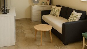 A living room with a sofa, a small round table, and a cabinet with a fan. - OLD RENOVATED COTTAGE NESTLED IN THE COUNTRYSIDE WITH GARDEN/RELAXATION CORNER (Adrano)