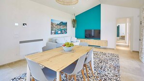 Ein modernes Wohnzimmer mit einem Holzesstisch, grauen Stühlen, einem großen Gemälde, einer türkisblauen Akzentwand und einem Fernseher.
