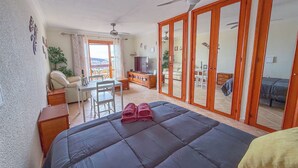 A bedroom with a bed, a desk, a chair, a TV, and a balcony with a view. - Port Royale Ocean Views Los Cristianos (Los Cristianos)