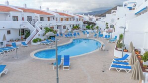 A poolside area with lounge chairs and a swimming pool, surrounded by white buildings with red-tiled roofs. - Port Royale Ocean Views Los Cristianos (Los Cristianos)