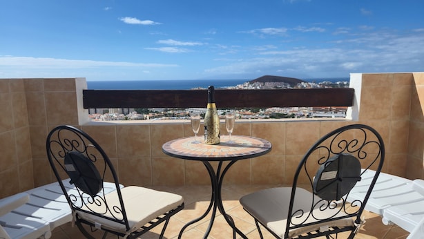 A balcony with a table and two chairs, a bottle of champagne, and a city view. - Port Royale Ocean Views Los Cristianos (Los Cristianos)