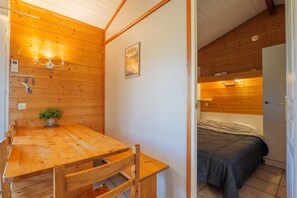 A wooden interior with a dining table, chairs, a bed, and a small potted plant.
