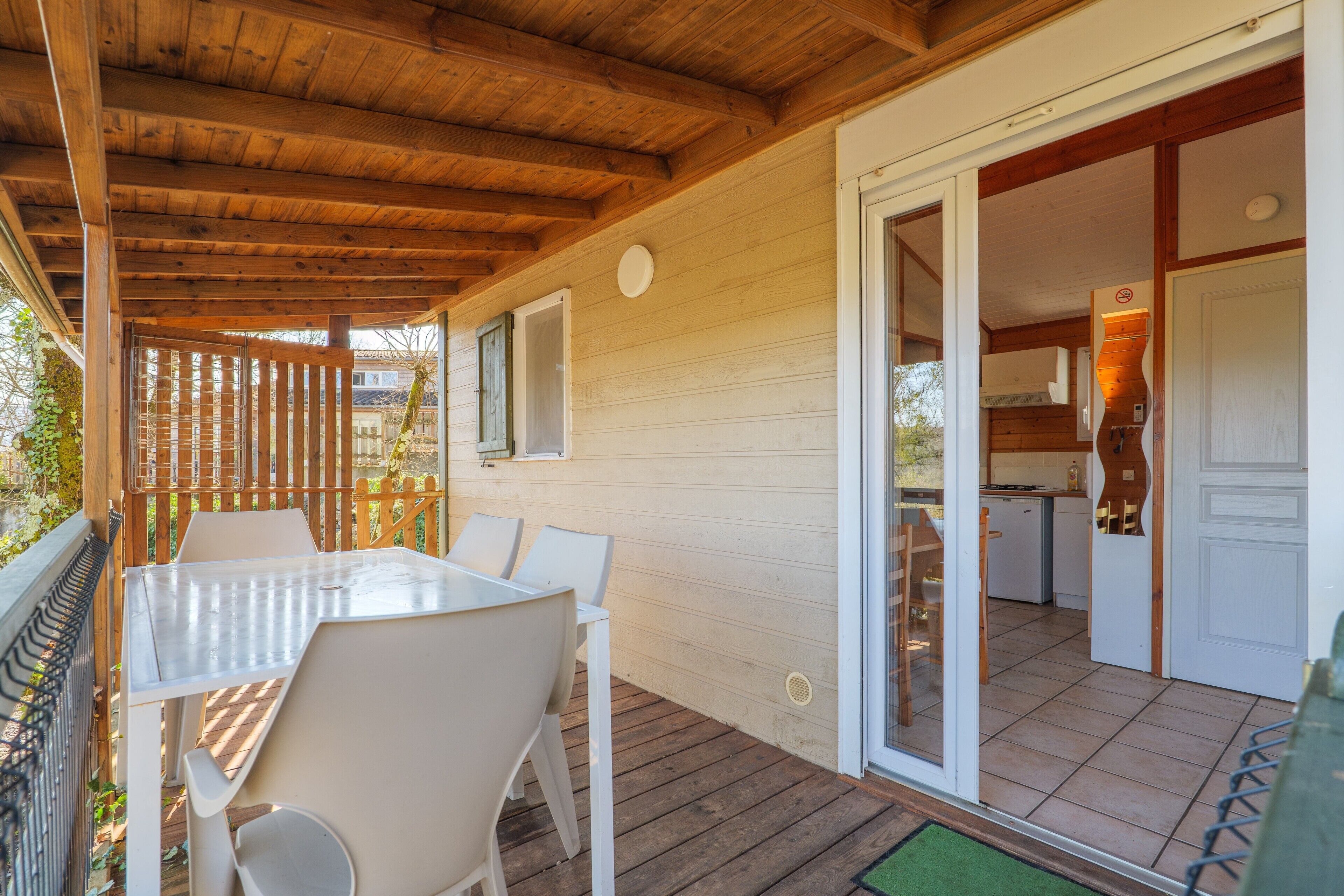 A covered outdoor area with a table and chairs, wooden deck, and a door leading to a kitchen.