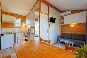A compact kitchen with a dining table, chairs, a gray sofa, and a TV mounted on the wall.