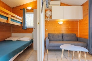 A wooden cabin with a bunk bed, a sofa, a small table, and a fan.