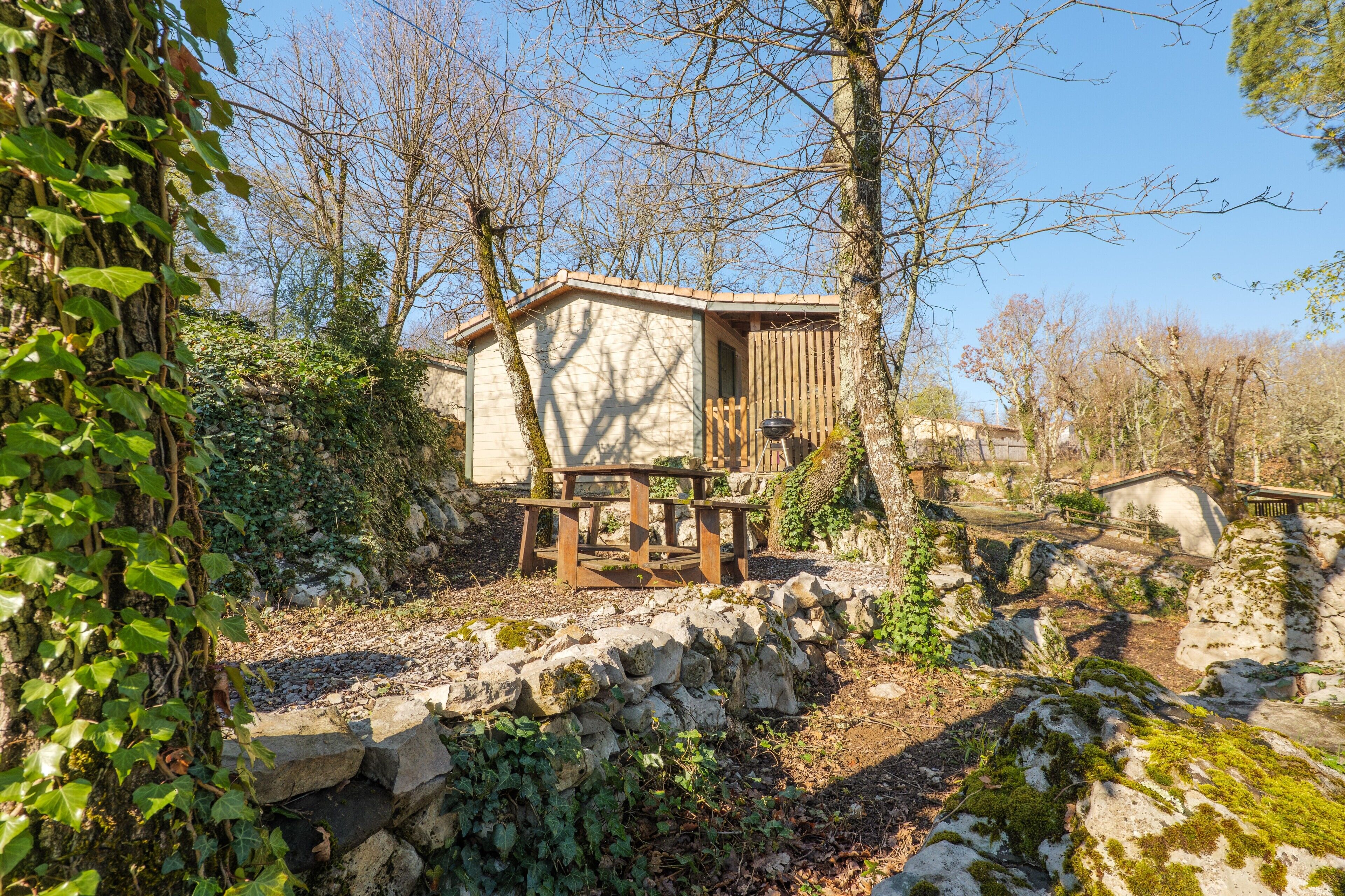 A rustic cabin with a stone wall, wooden deck, and a bench.