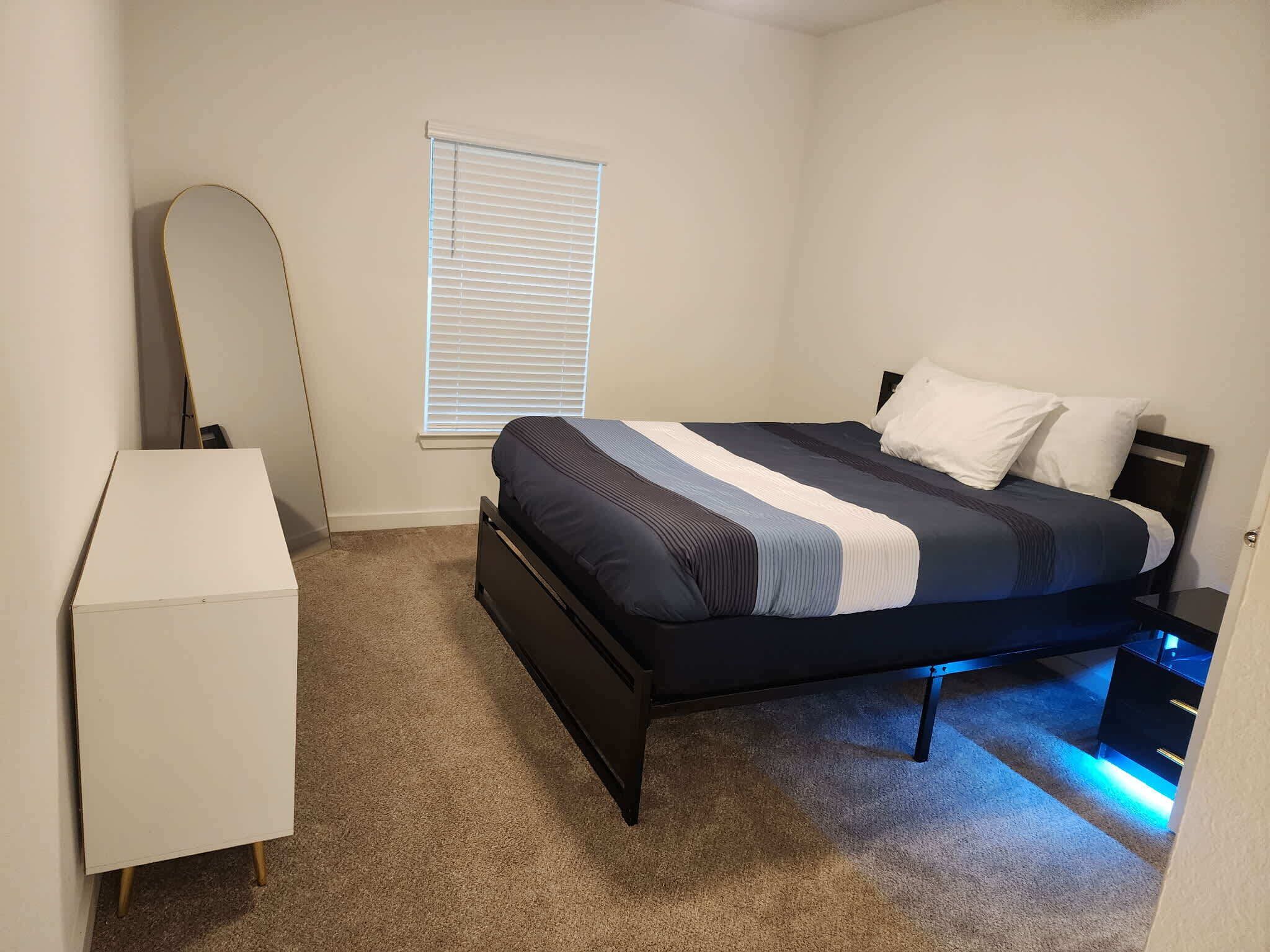 Un dormitorio con cama, cómoda, ventana con persianas y puerta.