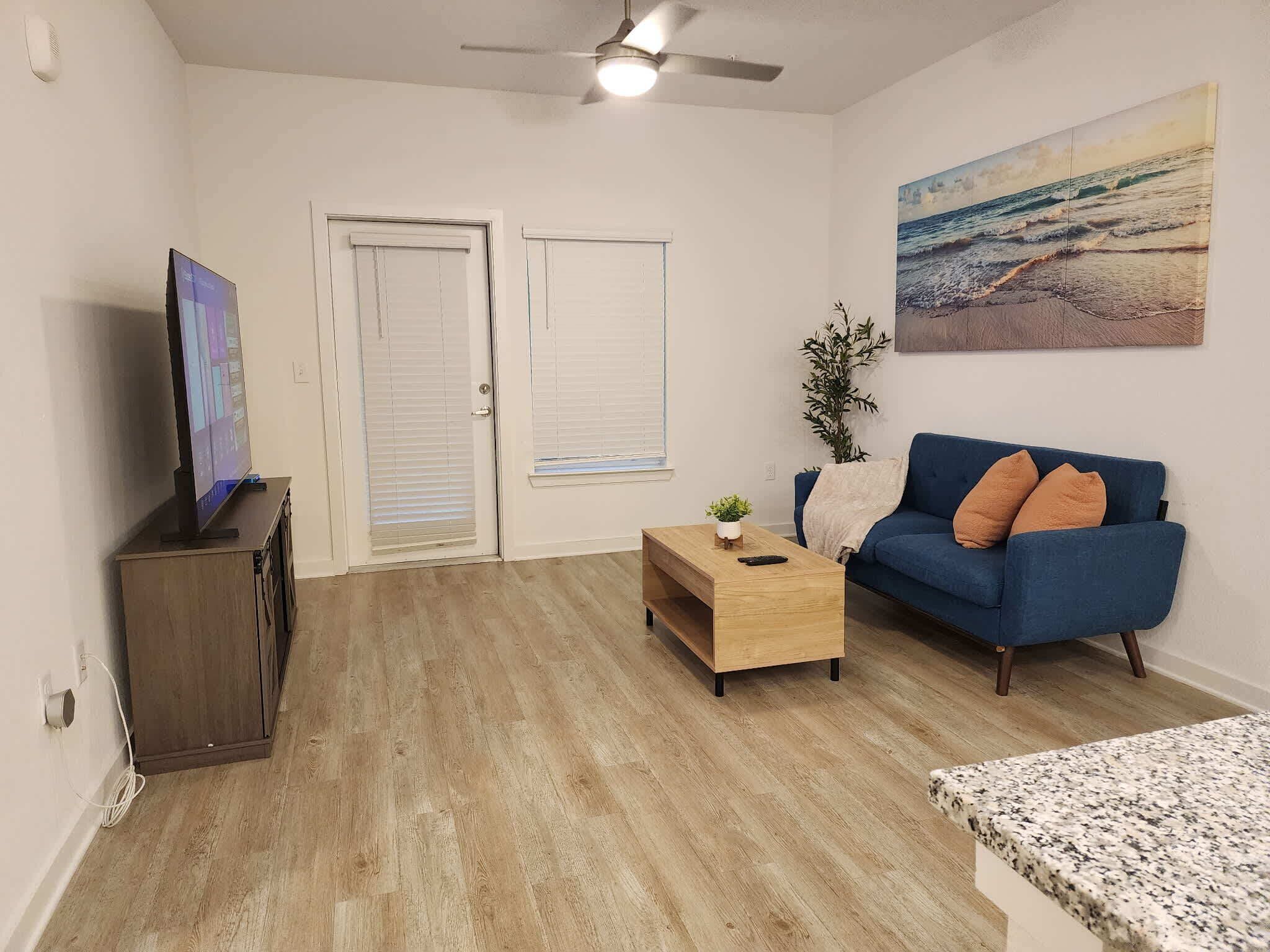 A living room with a blue sofa, a wooden coffee table, a television on a cabinet, and a painting on the wall.
