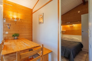 Ein Holzinterieur mit einem Esstisch, Stühlen, einem Bett und einem kleinen Topfpflanzen.