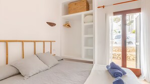 A bedroom with a bed, a wooden headboard, a built-in shelf with a woven basket, and a view of the outside through a glass door. - Apartment 'Villa Estrellas 2' with Shared Pool, Private Terrace, and Wi-Fi (Cap d'Artrutx)