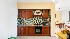 Une cuisine avec des meubles de rangement en bois, un pare-feu en carrelage, une cuisinière et un coin repas comprenant une table et des chaises.