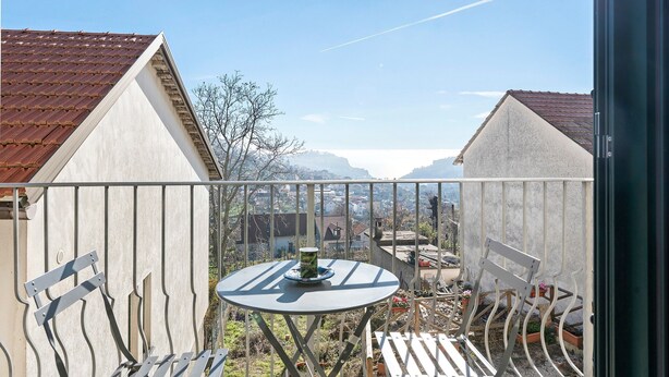Un balcon avec une table et des chaises, une vue sur une montagne et un ciel dégagé.