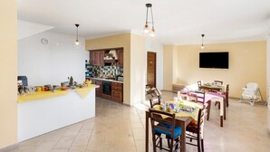 A spacious kitchen with a dining area, a TV mounted on the wall, and a small child’s chair. - Room 'Amalfi' with Sea View, Wi-Fi and Air Conditioning (Agerola)