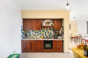 A kitchen with wooden cabinets, a tiled backsplash, a stove, and a dining area with a table and chairs. - Room 'Amalfi' with Sea View, Wi-Fi and Air Conditioning (Agerola)