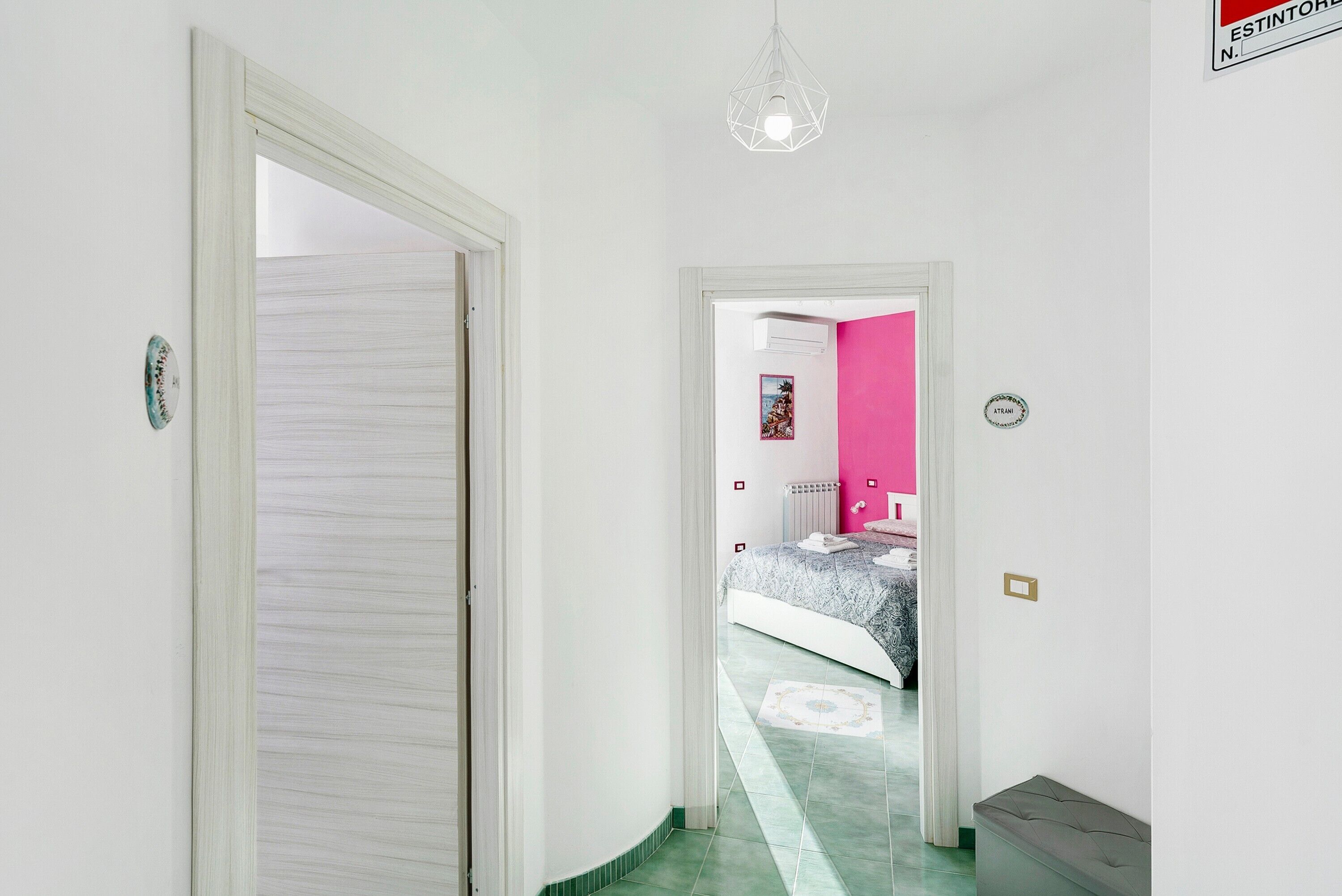 Ein Flur, der zu einem Schlafzimmer mit einem Bett, einem Heizkörper und einer rosafarbenen Wand führt.