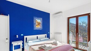 A bedroom with a large bed, a white bedside table, a blue accent wall, a framed picture, and a balcony with a view. - Room 'Amalfi' with Sea View, Wi-Fi and Air Conditioning (Agerola)