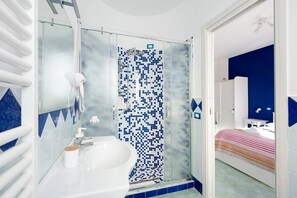 A bathroom with a shower, sink, and a bed in the adjacent room. - Room 'Amalfi' with Sea View, Wi-Fi and Air Conditioning (Agerola)