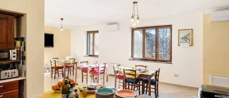 A dining area with a yellow tablecloth, chairs, and a variety of dishes and bottles. There are windows with views of the outside.