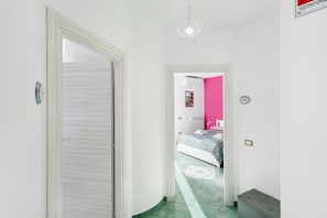 Een gang die leidt naar een slaapkamer met een bed, een radiator en een roze muur.