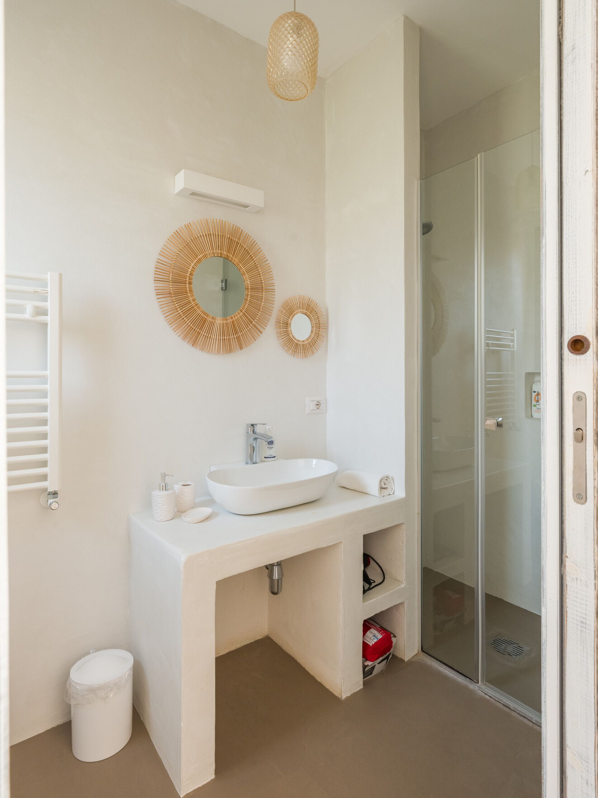 Une salle de bain moderne avec un lavabo blanc, deux miroirs fixés au mur, une douche et un espace de douche clos par des parois de verre.