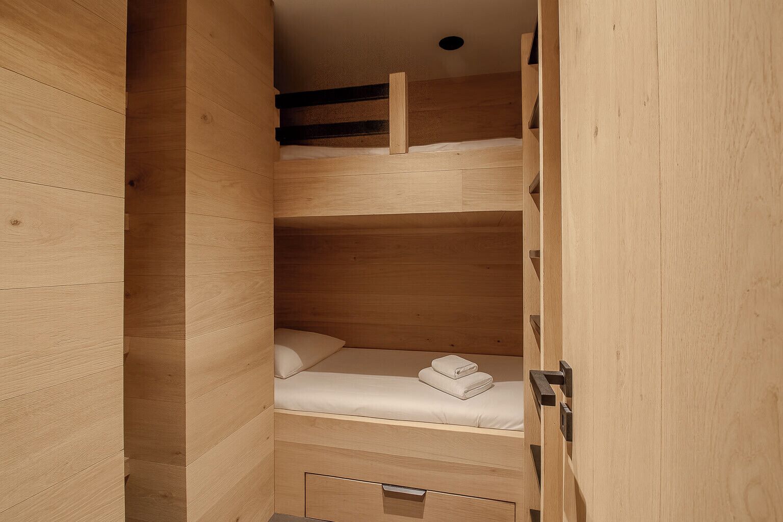 A wooden bunk bed room with a built-in wardrobe and a small storage cabinet.