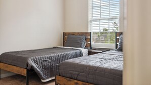 Ein Schlafzimmer mit zwei Einzelbetten, einem Fenster mit Jalousien und Blick auf Grün.