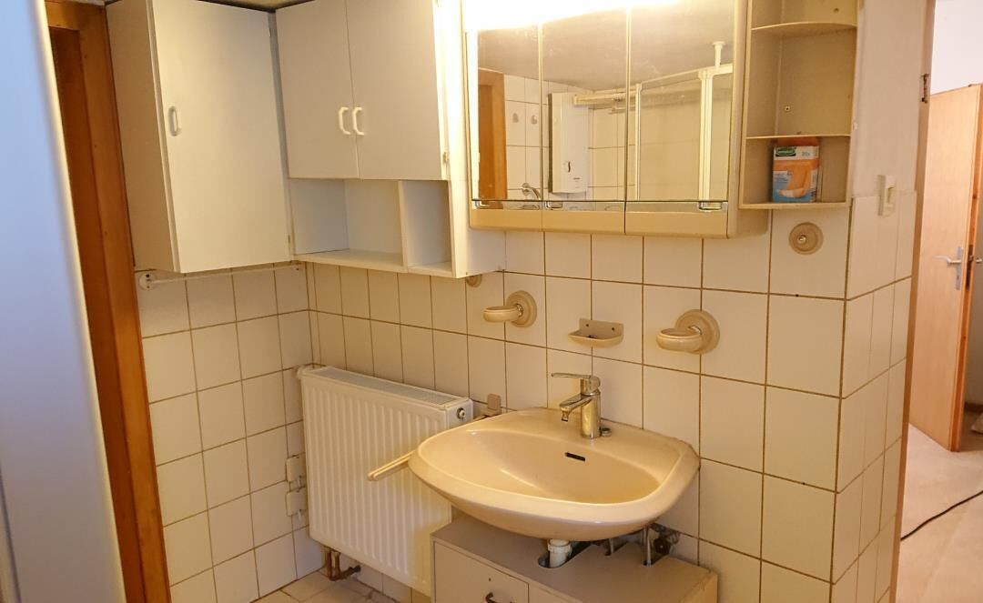 Un bagno con lavandino, specchio e mobiletti bianchi.