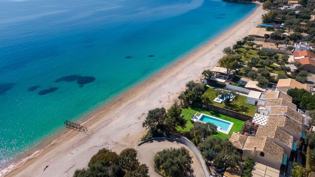 An aerial view of a coastal area with a beach, clear blue waters, and residential buildings with a swimming pool. - Barbati Beach - Villa Zante (Barbati)