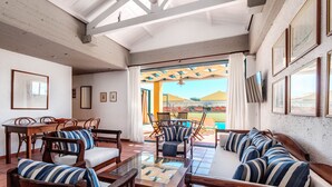 A spacious living area with a sofa, chairs, and a coffee table. There is a TV mounted on the wall and a view of the outside. - Barbati Beach - Villa Zante (Barbati)