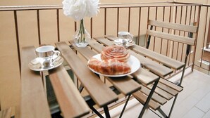 Une table en bois, sur laquelle se trouve une assiette de nourriture et une fleur blanche, est placée sur un balcon doté de rampes en métal.