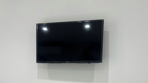 Un téléviseur à écran plat fixé à un mur blanc, une console blanche en dessous, ornée d’un vase de fleurs, et un magazine posé sur l’étagère inférieure.